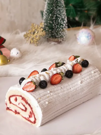 A beautiful white Christmas log cake. This strawberry swirl roll cake is covered in white frosting and topped with fresh berries for a light and festive treat.