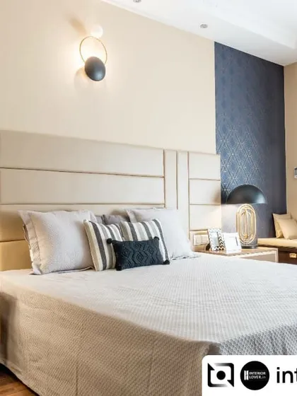 This master bedroom is a study in neutral elegance. The paneled upholstered headboard, combined with a textured blue accent wallpaper and modern light fixtures, creates a balanced and restful environment.