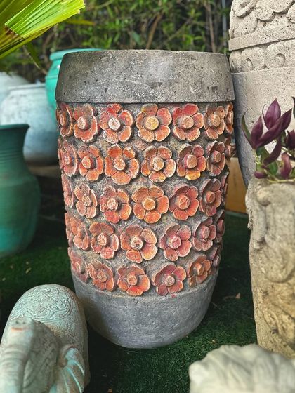 This stone planter features rows of carved flowers with a hint of color, adding a playful and artistic touch to your garden.