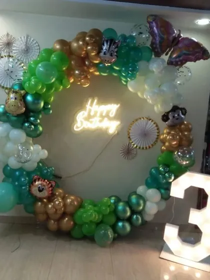 A jungle-themed ring decoration with green and gold balloons, animal foil balloons, and a 'Happy Birthday' neon sign.
