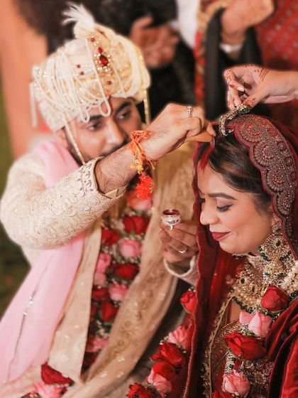 A close up of the Maang Bharai ritual. This image focuses on the groom's hand as he applies sindoor, a deeply symbolic and intimate moment in a Hindu wedding ceremony.