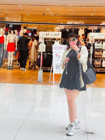 A mirror selfie in a store, wearing a black dress and a light-colored cardigan, a perfect casual layering example.