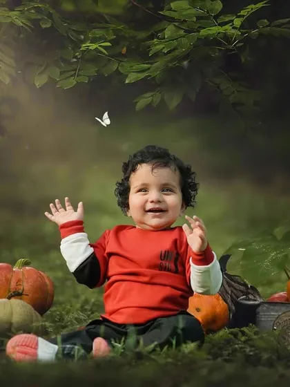 A happy little boy surrounded by pumpkins and autumn colors. His joyful wave and the magical butterfly create a perfect fall-themed portrait.