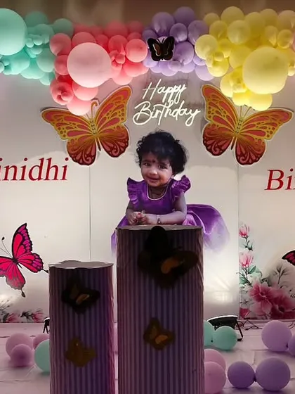A beautiful butterfly-themed first birthday for Sriinidhi. The centerpiece is a photo of the birthday girl on a pedestal, framed by a colorful rainbow balloon arch and accented with monarch butterfly details.