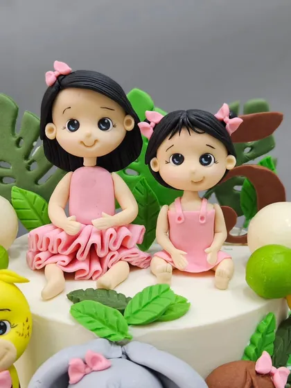 A close-up of the two sister figurines from a combined jungle-themed birthday cake. Personalizing cakes with figures that look like the birthday girls makes the celebration extra special.