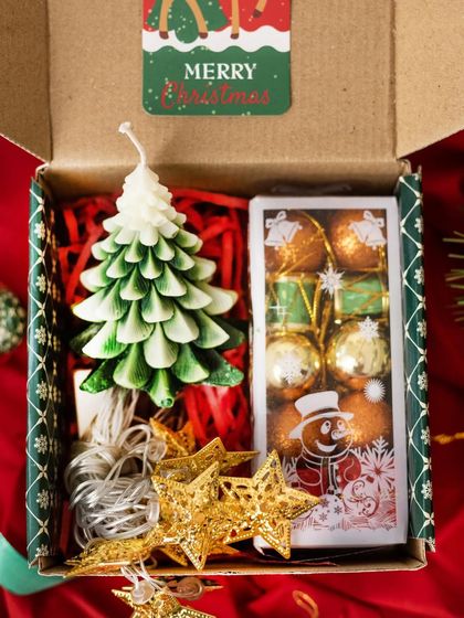 A beautiful and aromatic Christmas gift, this box features a tree-shaped candle, a string of star-shaped fairy lights, and a box of festive chocolates.