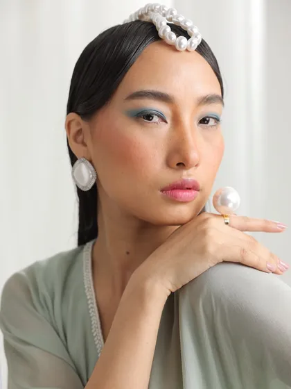 A campaign shot focused on pearl accessories. The model's pastel green outfit and soft makeup complement the oversized pearl ring and headpiece, creating a look of modern opulence.