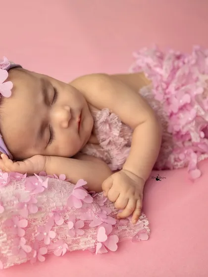 Dressed in a beautiful pink floral outfit, this baby girl sleeps soundly on her side. The soft lighting and textures create a dreamy and gentle atmosphere.