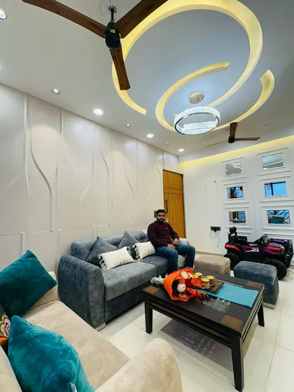 A completed living room at Nirala Estate, featuring a comfortable sofa, a 3D paneled accent wall, and a stylish false ceiling design.