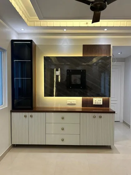 A modern TV and entertainment unit we designed and built. It features a combination of white fluted cabinets, sleek drawers, and a dark wood top, all set against a marble-look backdrop for the television. The integrated backlighting adds a warm, ambient glow.