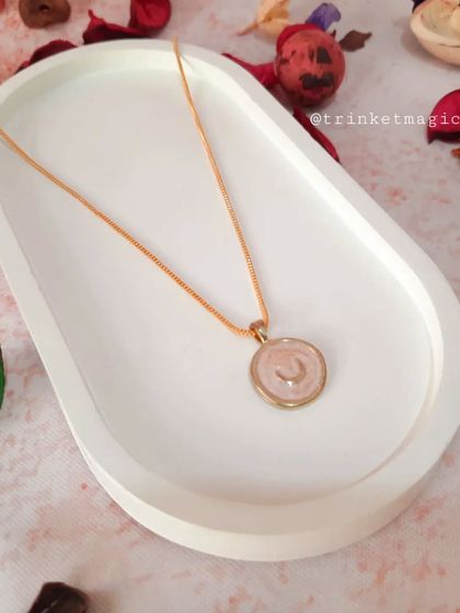 Add a cosmic touch to your look with this celestial moon pendant necklace. The delicate pink enamel and gold chain create a dreamy accessory.