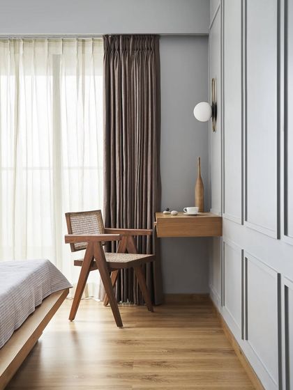 The classic Chandigarh chair with rattan cane webbing sits in a sunlit corner, providing a perfect spot for reading. It's a timeless piece that complements the room's modern, minimal aesthetic.