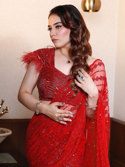 A close-up of a client in a stunning red draped saree with a feather-detailed blouse. The sequin work adds a beautiful sparkle.
