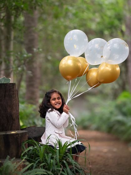 A candid shot of pure joy as she holds onto her balloons. You can feel the happiness radiating from her smile in this outdoor portrait.