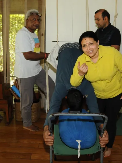 A student receives assistance in a forward bend using a chair and a bolster. This shows the collaborative and supportive environment of my classes, where props and teachers work together to help you achieve your best.