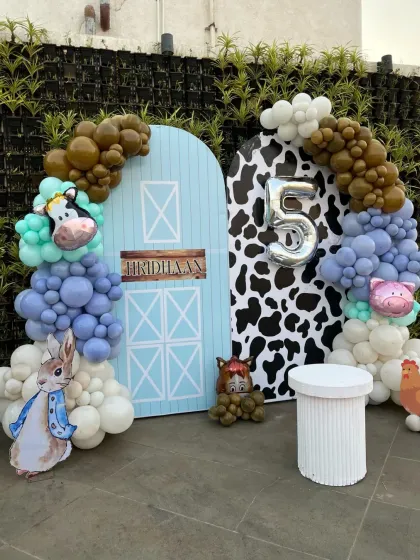 The backdrop for the farm party features a barn door, cow-print panel, and animal-themed balloon details, perfect for a 5th birthday.