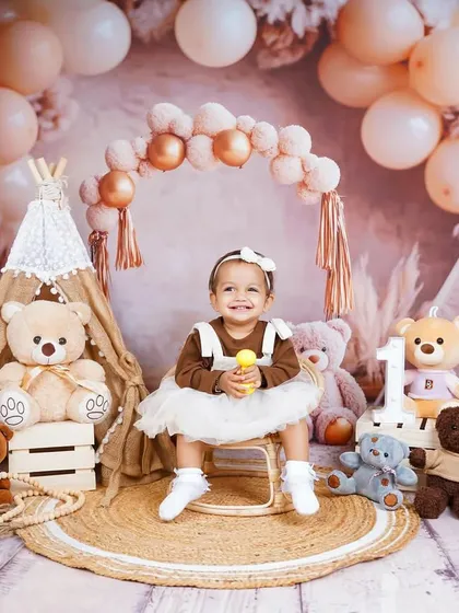 A sweet smile while holding a toy. The variety of textures, from the jute rug to the soft balloons, adds depth to the photograph.
