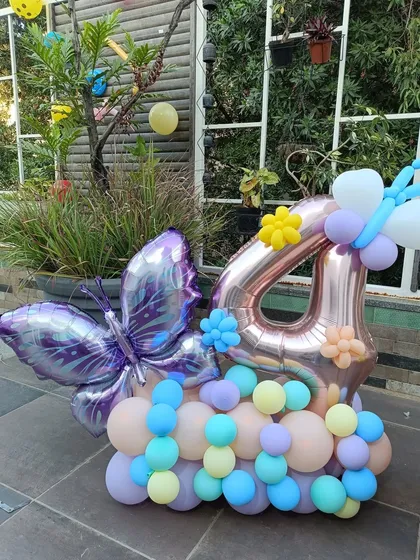 A charming balloon arrangement for a 4th birthday, featuring a large rose gold number '4' balloon. It's decorated with a pastel balloon cluster, a foil butterfly, and small balloon flowers for a whimsical touch.