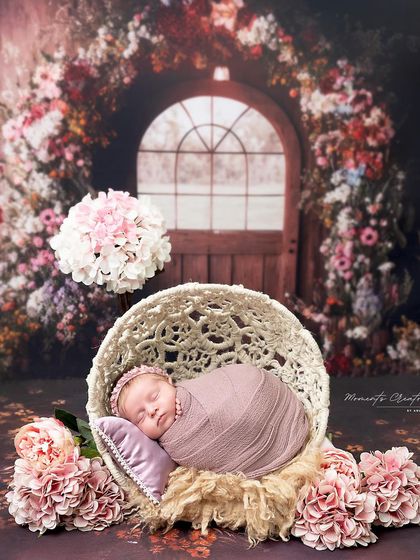 A floral dream. This newborn girl sleeps in a beautiful crocheted basket, set against a magical backdrop of a flower-covered doorway.