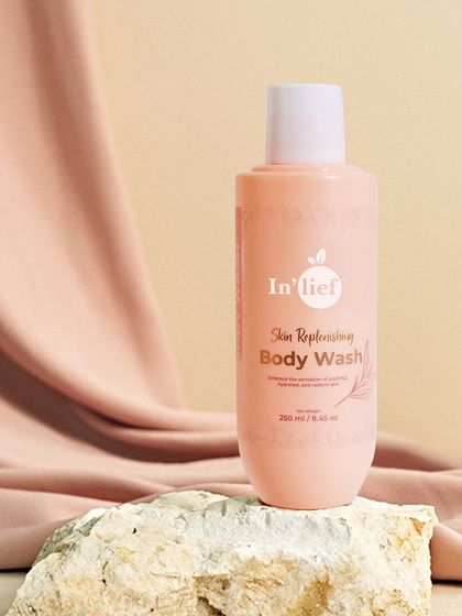 A styled shot of In'lief body wash resting on natural stone with draped fabric. The textures and soft colors create a gentle, soothing mood.