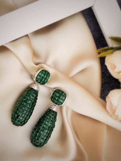 The deep green, textured surface of these emerald earrings is beautifully complemented by the soft, flowing silk. This simple, elegant styling allows the luxurious details of the jewelry to be the main focus.