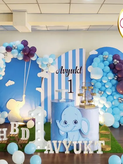 A dreamy baby elephant theme for a first birthday. This setup features a large hot-air-balloon-style balloon sculpture, a 'ONE' marquee number, and a personalized milestone board.