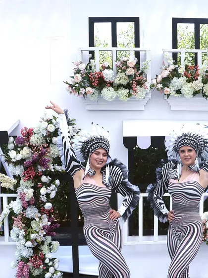 Performers pose in front of a European-style facade with window boxes, adding to the charming and sophisticated atmosphere of the black-and-white carnival.