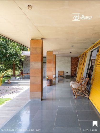 The long, covered walkway of the Aamra residence, flanked by compressed stabilized earth block (CSEB) pillars. The design provides shelter from the elements while maintaining a constant visual and physical connection to the lush landscape.
