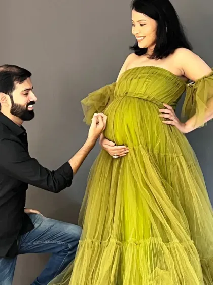 A tender moment between parents-to-be. Our olive green off-shoulder tulle gown adds a touch of soft elegance to this studio maternity session, perfectly complementing the partner's classic black shirt for a coordinated look.