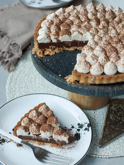 A slice of the Chocolate & Espresso Tart, revealing the crisp shortbread crust and the silky chocolate filling beneath the coffee-flavored cream.