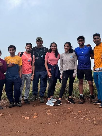 A happy group of trekkers on a dirt trail, with rolling green hills behind them. Every trek is an opportunity to meet your next adventure buddies.