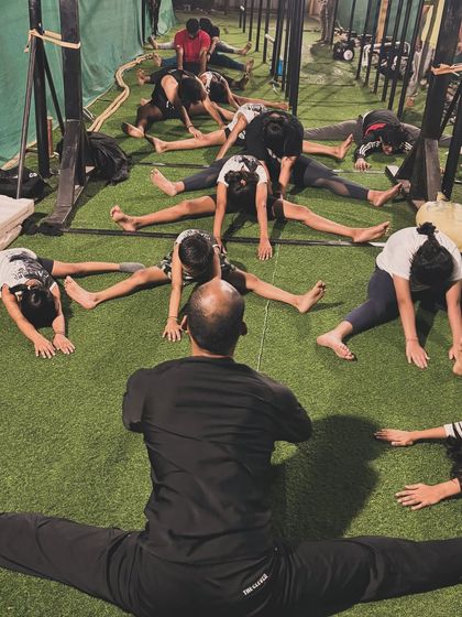 Our head coach leads by example, demonstrating a full center split while the class follows along. We believe in practicing what we preach.