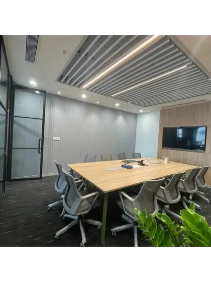 A formal meeting room with a large conference table, ergonomic chairs, and a wall-mounted display. The slatted ceiling and textured wall panels provide acoustic dampening, essential for a functional conference space.
