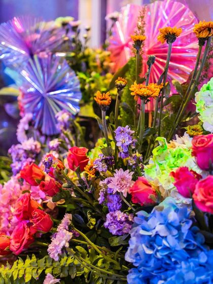 A macro shot of the floral arrangement, showing the rich mix of colors and textures, from blue hydrangeas and purple statice to bright orange marigolds.