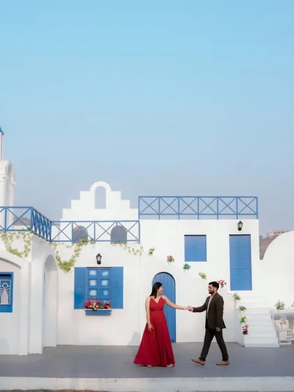 A grand, cinematic shot at a Santorini-inspired location in Pune. The sweeping view of the white and blue architecture creates a breathtaking backdrop for a romantic pre-wedding photo.