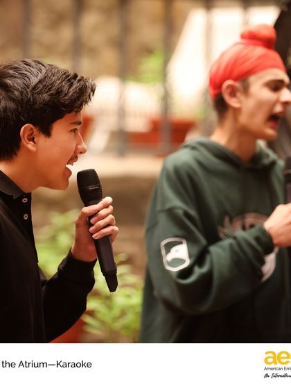Two students passionately sing a duet during 'Arts in the Atrium: Karaoke'. We encourage students to be fearless in their self-expression and support each other's performances.
