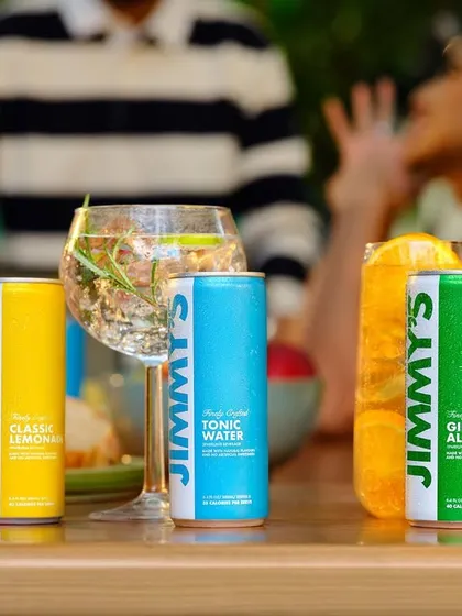 A close-up of the Jimmy's Cocktail product line on a table during a party. This shot clearly displays the different flavors available while keeping the fun, social atmosphere of the campaign visible.