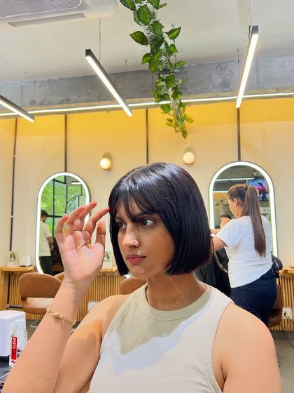 A client selfie showing off her new short haircut with bangs. The cut is tailored to her face shape for a flattering result.