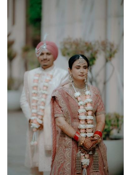A creative shot with the bride in focus and the groom slightly behind her, both adorned with beautiful varmalas.