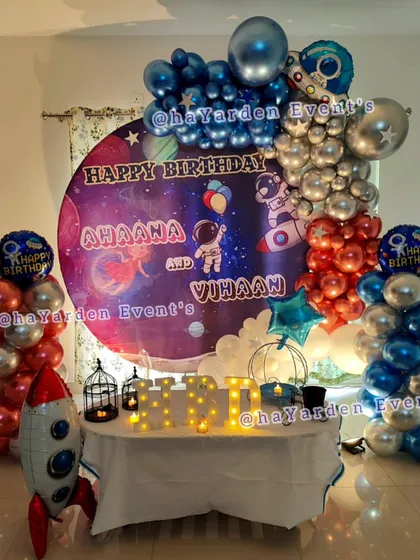 A complete space-themed birthday setup with a large galaxy backdrop, rocket ship foil balloons, and balloon pillars.