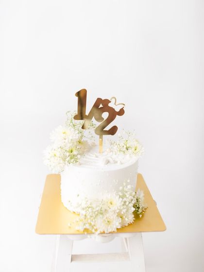 A close-up of the beautiful cake for a six-month birthday celebration, complete with a "1/2" topper and delicate white flowers.