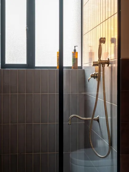 The details make the design. In this bathroom, the antique-style brass faucet and shower fixtures add a touch of vintage charm against the modern, vertically stacked grey tiles. The light from the window creates a soft, calming glow.