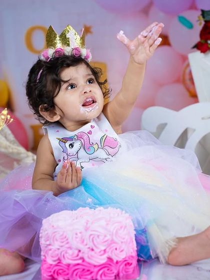 Reaching for the sky, or maybe just more cake! This photo captures the playful energy and happiness of a first birthday celebration.