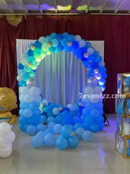 A blue and white themed baby shower or welcome baby boy decoration, featuring a circular balloon arch and 'BABY' blocks.