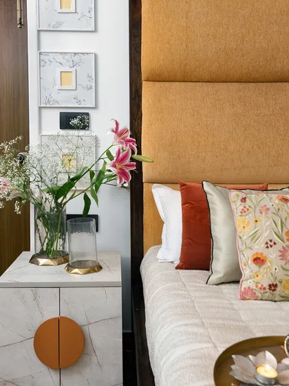 A close-up of a custom bedside table with a marble-effect finish and a warm, circular handle. The textures of the upholstered headboard, fresh flowers, and curated art pieces come together to create a soft and inviting corner.