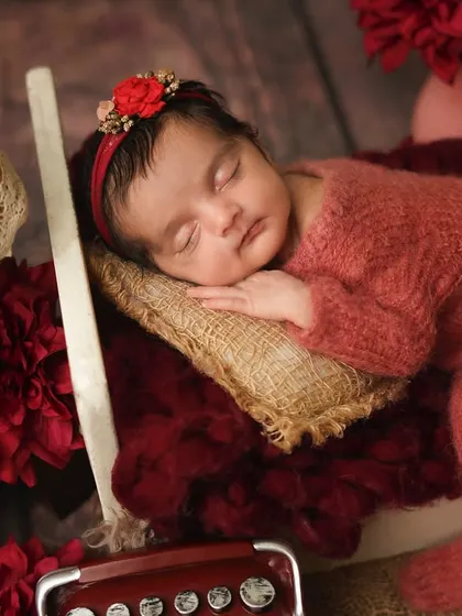 A side view of the newborn in her red-themed bed, showing her sweet sleeping profile.