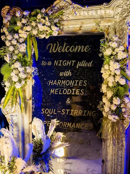 An opulent welcome sign on a silver-framed mirror, adorned with white flowers, perfect for a glamorous Sangeet or reception.