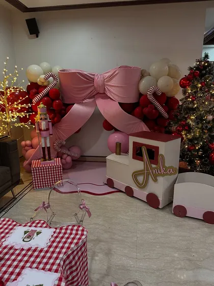 The complete setup for Anika's Christmas house party, featuring a festive backdrop with a giant pink bow, a custom train prop, and a beautifully decorated tree.