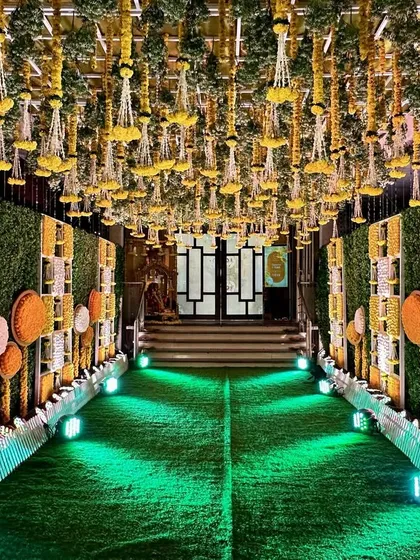 A beautiful entrance passage for a Haldi ceremony. The walls and ceiling are adorned with a canopy of yellow florals and greenery, creating a lush and sunny walkway.