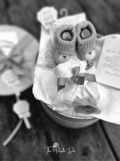A soft-focus, black and white photograph of the hamper's contents, emphasizing the cozy textures of the knitted booties and soft swaddle.